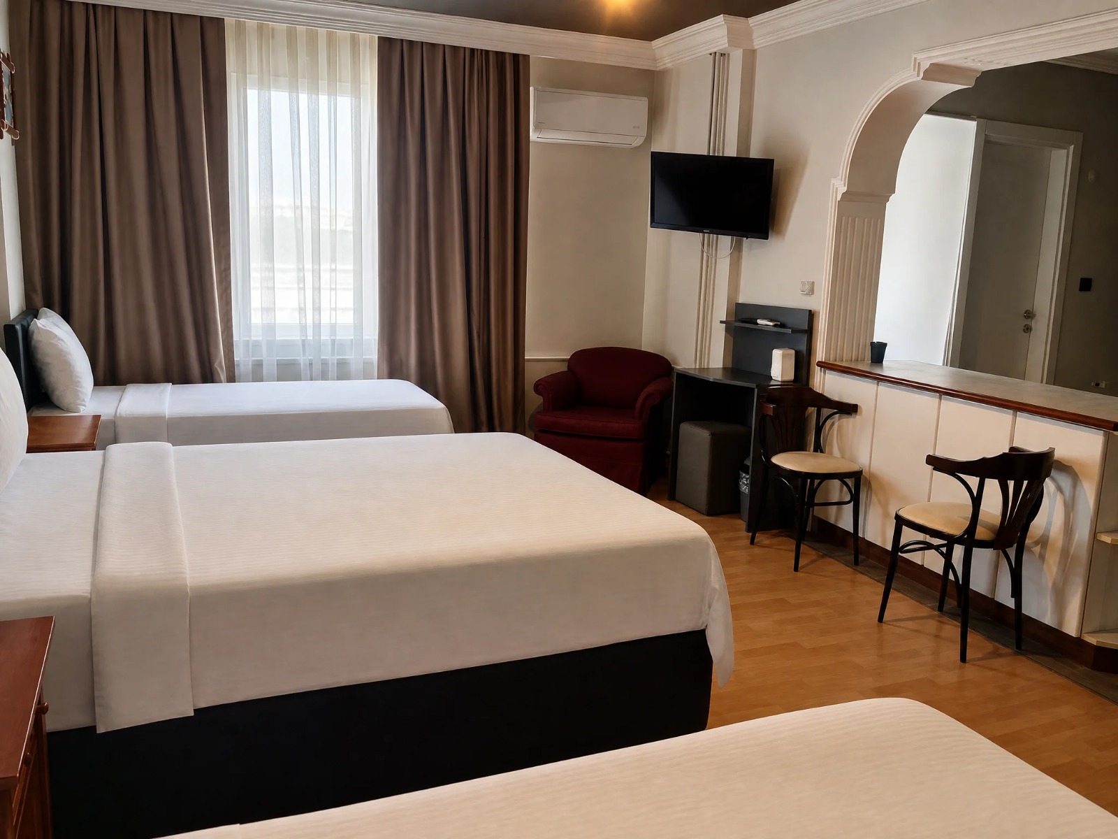 Üç kişilik odada iki yatak, çalışma masası ve bordo koltuk